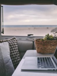 Remote onilne work and smart working travel concept with laptop computer inside a van camper interior with beach view. Freedom from office modern lifestyle for alternative life and people